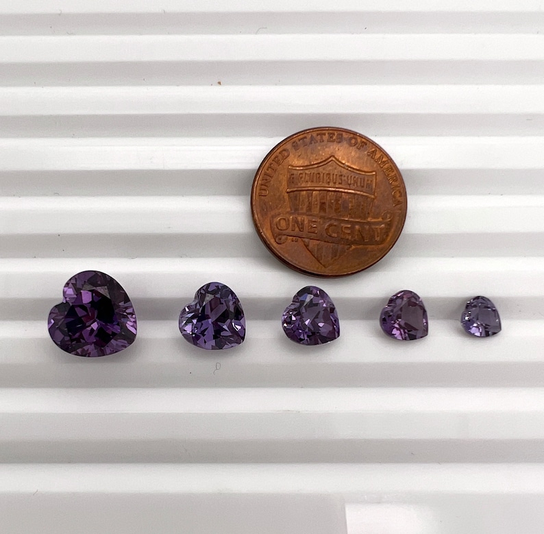 K&ouml;nnte beinhalten: F&uuml;nf herzf&ouml;rmige Amethyst-Edelsteine ​​in verschiedenen Gr&ouml;&szlig;en, der gr&ouml;&szlig;te ist etwa so gro&szlig; wie ein 1-Cent-St&uuml;ck.