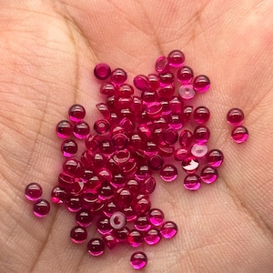 May include: A pile of small, round, bright pink ruby beads.