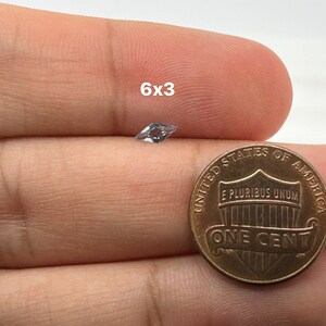 Peut inclure: Une pierre pr&eacute;cieuse transparente et facet&eacute;e, mesurant 6x3, est tenue dans une main &agrave; c&ocirc;t&eacute; d'un penny am&eacute;ricain pour comparaison de taille.