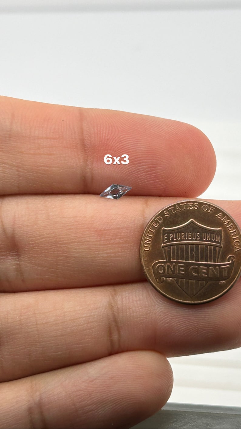 Peut inclure: Une pierre pr&eacute;cieuse transparente et facet&eacute;e, mesurant 6x3, est tenue dans une main &agrave; c&ocirc;t&eacute; d'un penny am&eacute;ricain pour comparaison de taille.