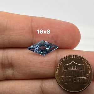 Peut inclure: Une pierre pr&eacute;cieuse bleu clair en forme de cerf-volant, mesurant 16x8, est tenue dans une main &agrave; c&ocirc;t&eacute; d'un penny am&eacute;ricain pour comparaison de taille.