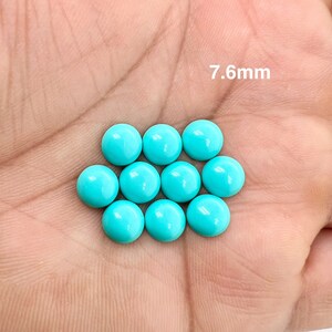 May include: Ten turquoise round cabochon gemstones, each measuring 7.6mm in diameter, are displayed on a hand.