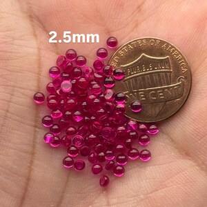 May include: A pile of 2.5mm round ruby red glass beads next to a US one cent coin.