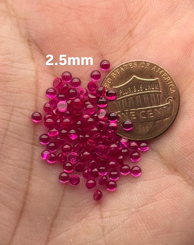 May include: A pile of 2.5mm round ruby red glass beads next to a US one cent coin.
