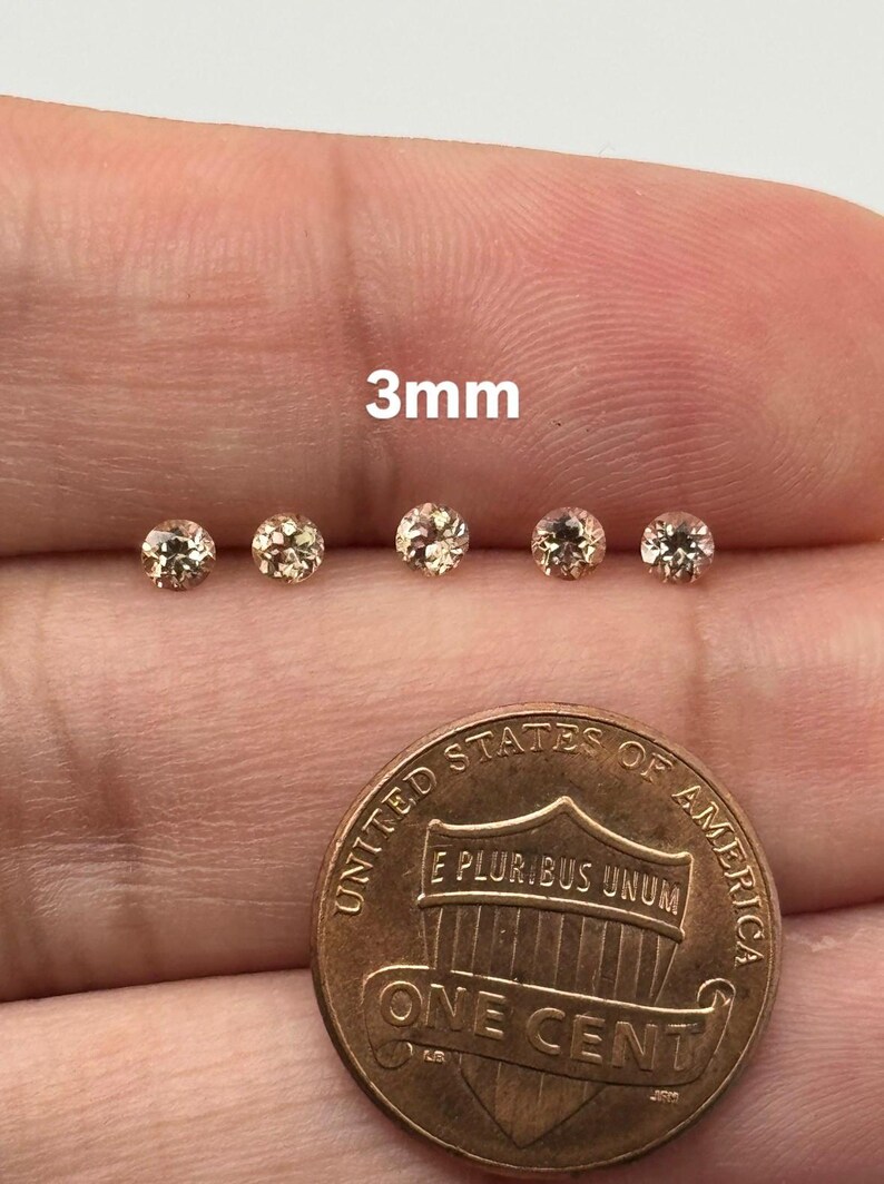May include: Five small, round, light-colored gemstones, each approximately 3mm in diameter, are displayed next to a United States one-cent coin. The text "3mm" is visible above the gemstones.
