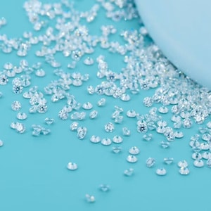Könnte beinhalten: Nahaufnahme einer Streuung kleiner, klarer Diamanten auf einer hellblauen Oberfläche. Die Diamanten sind in verschiedenen Größen und Formen und funkeln im Licht.