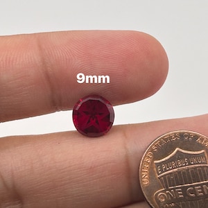 May include: A 9mm red star-shaped gemstone with a faceted cut. The gemstone is held in a hand for size comparison.