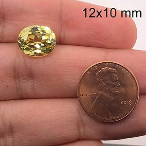 May include: A yellow oval gemstone measuring 12x10 mm, next to a UK penny for size comparison.