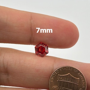 May include: A 7mm red hexagonal gemstone, shown next to a US penny for size comparison.