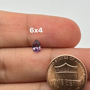 May include: A pear-shaped purple gemstone measuring 6x4 millimeters, shown next to a US penny for size comparison.