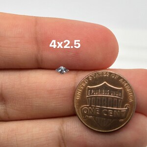 Peut inclure: Une petite pierre pr&eacute;cieuse carr&eacute;e transparente est tenue dans une main &agrave; c&ocirc;t&eacute; d'une pi&egrave;ce de monnaie am&eacute;ricaine d'un cent. La pierre pr&eacute;cieuse mesure environ 4 mm x 2,5 mm.
