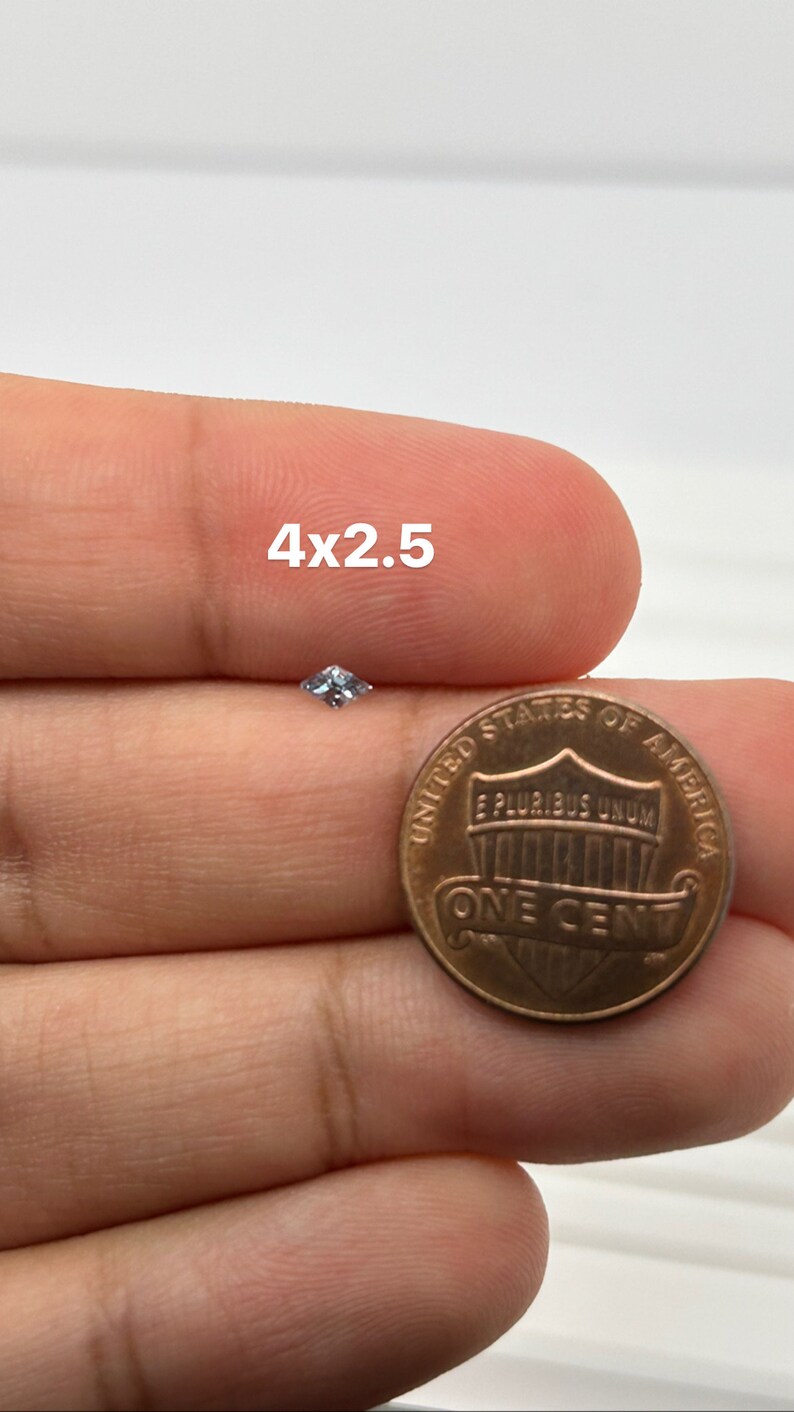Peut inclure: Une petite pierre pr&eacute;cieuse carr&eacute;e transparente est tenue dans une main &agrave; c&ocirc;t&eacute; d'une pi&egrave;ce de monnaie am&eacute;ricaine d'un cent. La pierre pr&eacute;cieuse mesure environ 4 mm x 2,5 mm.