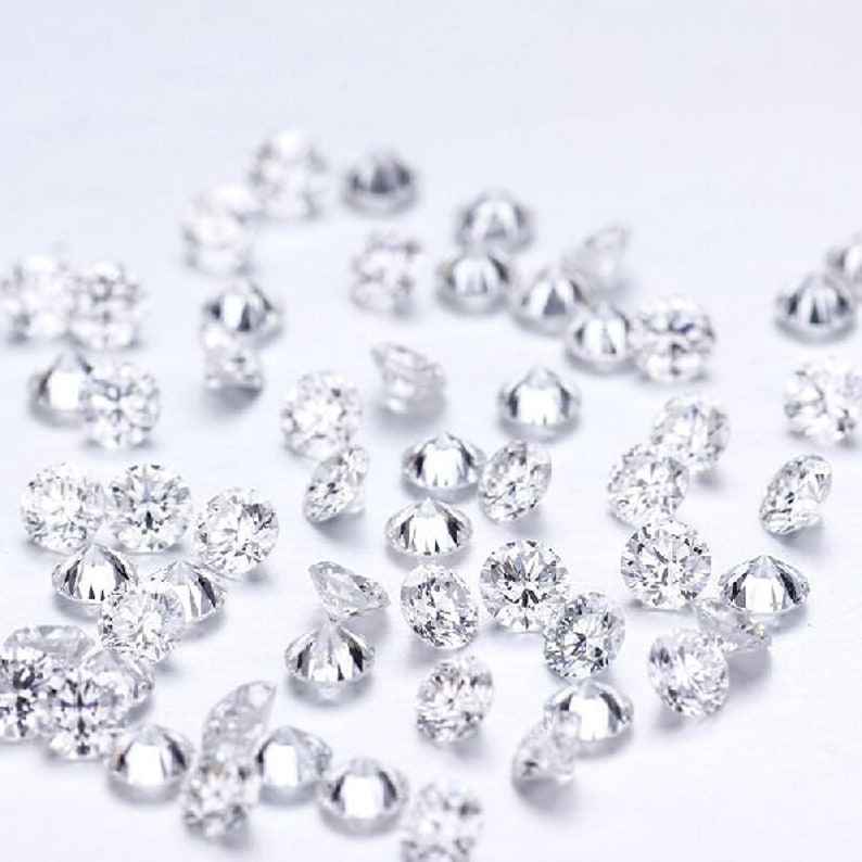 Puede incluir: Una colecci&oacute;n de diamantes sueltos, redondos y transparentes esparcidos sobre una superficie blanca.