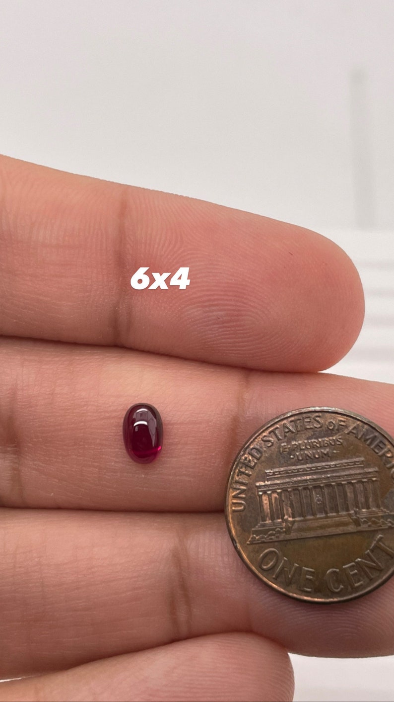 K&ouml;nnte beinhalten: Ein ovaler, dunkelroter Edelstein mit den Ma&szlig;en 6x4 mm, neben einem US-Cent zur Gr&ouml;&szlig;enveranschaulichung.