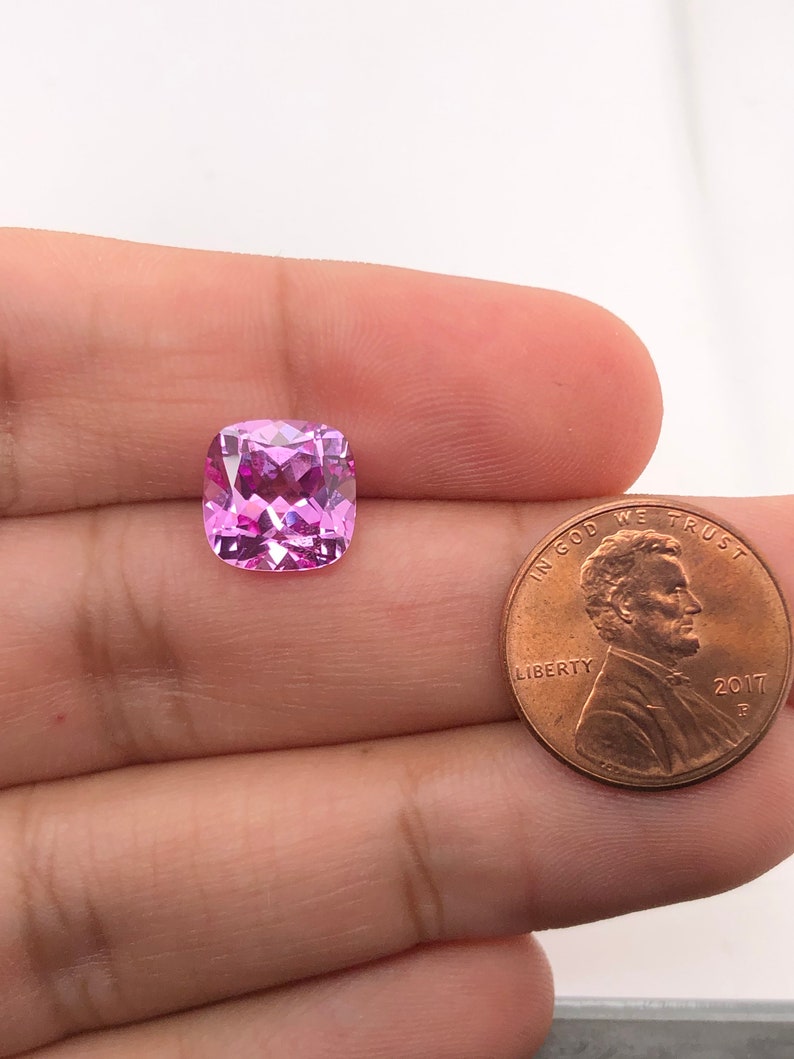 May include: A pink cushion-cut gemstone, approximately the size of a US penny.