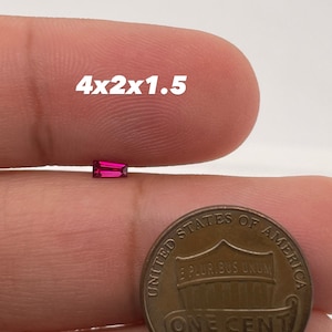 Op de afbeelding: Een close-up van een helderrode edelsteen, met een afmeting van 4x2x1,5, naast een Amerikaanse penny ter vergelijking van de grootte.