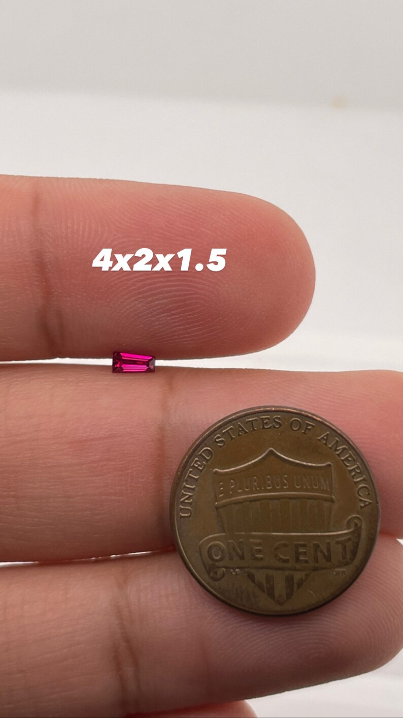 Op de afbeelding: Een close-up van een helderrode edelsteen, met een afmeting van 4x2x1,5, naast een Amerikaanse penny ter vergelijking van de grootte.