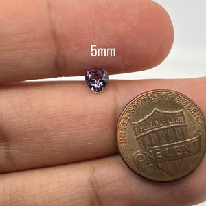 K&ouml;nnte beinhalten: Ein lilafarbener herzf&ouml;rmiger Edelstein mit einem Durchmesser von 5 mm. Der Edelstein wird von einer Hand gehalten, mit einem US-Penny als Gr&ouml;&szlig;envergleich.