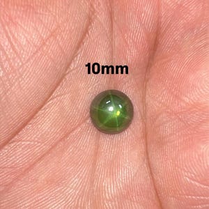 May include: A round, green gemstone, approximately 10mm in diameter, rests in an open palm. The gem has a star-like pattern within. The text "10mm" is displayed above the gem.
