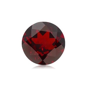 May include: A round, red gemstone with a faceted cut. The gemstone is set against a white background.