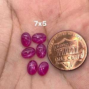 Puede incluir: Seis piedras preciosas de rubí estrella rosa, cada una con un patrón en forma de estrella, se muestran en una mano. Las piedras preciosas miden aproximadamente 7x5 milímetros. Un centavo de dólar estadounidense se incluye para la comparación de tamaño.
