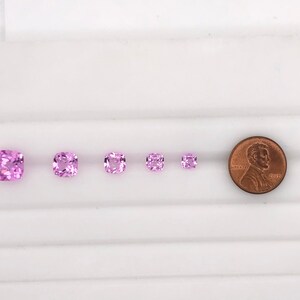 May include: Five pink square-shaped gemstones of varying sizes, arranged in a row from largest to smallest. A penny is included for scale.