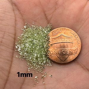 May include: A pile of 1mm green glitter next to a US penny. The penny is a copper coin with the words "One Cent" and "United States of America" on it.
