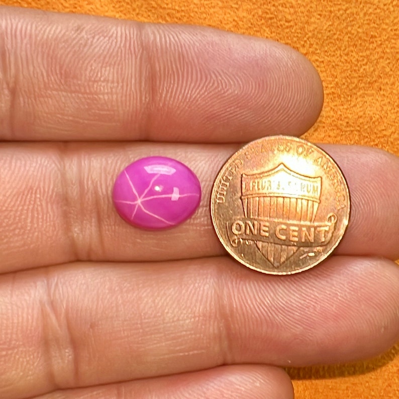 Puede incluir: Una piedra preciosa de rub&iacute; estrellado rosa con un patr&oacute;n de estrella, junto a un centavo estadounidense para comparar el tama&ntilde;o.