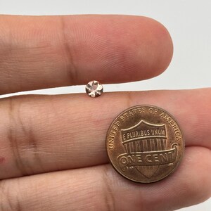 Op de afbeelding: Een kleine, ronde, lichtroze edelsteen op een vinger, naast een Amerikaanse cent ter groottevergelijking.
