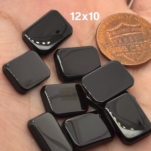 May include: A group of eight black rectangular glass tiles, each measuring 12x10 inches, are displayed on a hand. The tiles are smooth and glossy.