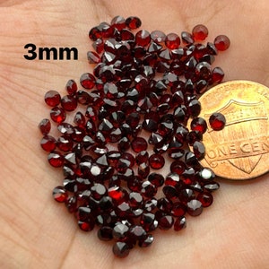 May include: A pile of 3mm red garnet gemstones, shown next to a US penny for size comparison.