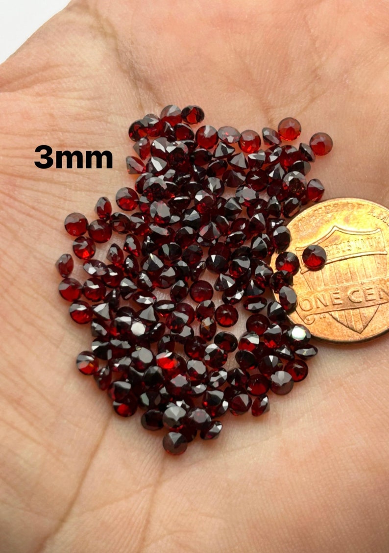 May include: A pile of 3mm red garnet gemstones, shown next to a US penny for size comparison.