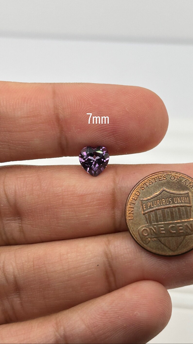 K&ouml;nnte beinhalten: Ein 7 mm gro&szlig;er herzf&ouml;rmiger violetter Edelstein, neben einem US-Penny zum Gr&ouml;&szlig;envergleich.