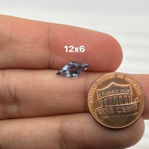 Peut inclure: Une pierre pr&eacute;cieuse bleu clair de forme cerf-volant, mesurant 12x6 mm, est tenue dans une main &agrave; c&ocirc;t&eacute; d'un centime am&eacute;ricain pour comparaison de taille.