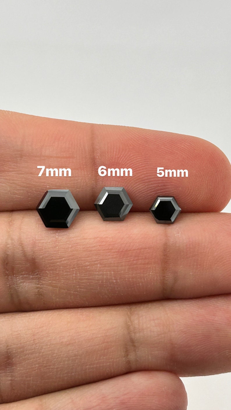 May include: Three black hexagonal diamonds, 7mm, 6mm, and 5mm in size, are displayed on a finger.