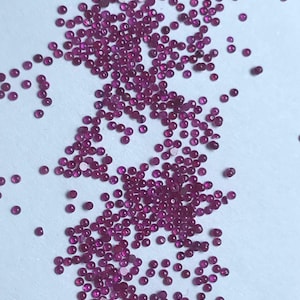 May include: A scattering of small, round, ruby red gemstones on a white background.