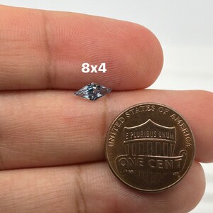 Peut inclure: Une pierre pr&eacute;cieuse bleu clair de forme rectangulaire, mesurant 8x4 millim&egrave;tres, est tenue dans une main &agrave; c&ocirc;t&eacute; d'un penny am&eacute;ricain pour comparaison de taille.