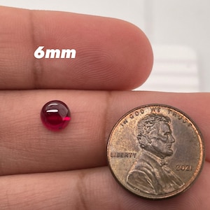 May include: A 6mm red gemstone cabochon next to a 2021 UK penny. The penny is used for size comparison.