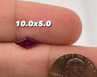 May include: A deep red gemstone with a kite shape, measuring 10.0 x 5.0, is held in a hand next to a US penny for size comparison.