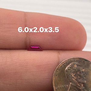 Puede incluir: Una piedra preciosa rectangular de color rojo intenso que mide 6,0x2,0x3,5 pulgadas, sostenida en una mano junto a un centavo estadounidense.