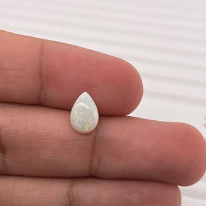 May include: A white teardrop-shaped opal gemstone with iridescent flashes of color.