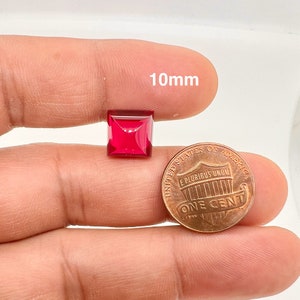 Op de afbeelding: Een vierkante rode edelsteen van 10 mm, getoond naast een Amerikaanse cent ter vergelijking van de grootte.