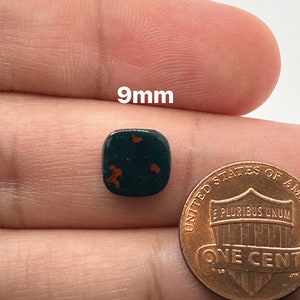 May include: A 9mm green and red jasper cabochon, a square-shaped gemstone with a polished surface, next to a US penny for size comparison.