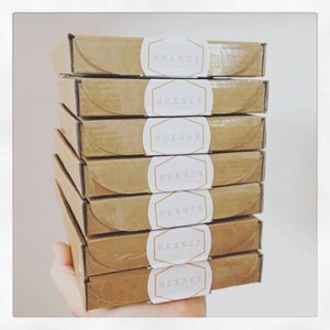 May include: A stack of seven brown cardboard boxes with white circular labels that say "HEXNEX" in gold lettering.
