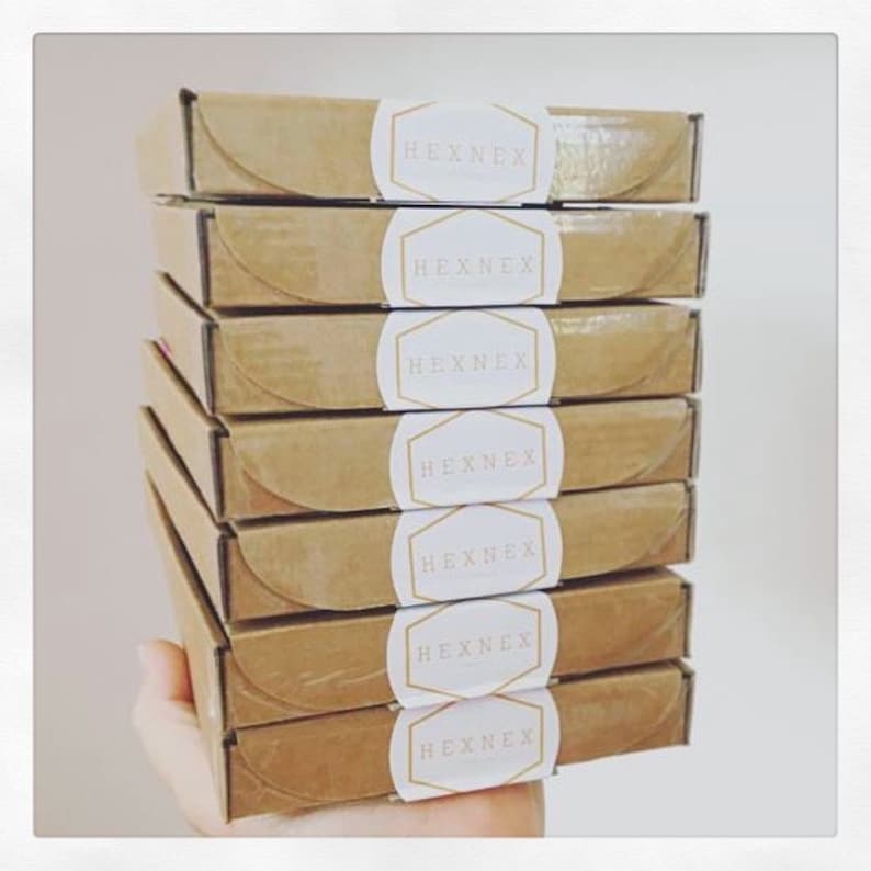 May include: A stack of seven brown cardboard boxes with white circular labels that say "HEXNEX" in gold lettering.