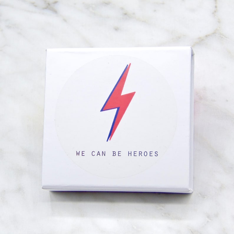 May include: White box with a red lightning bolt graphic and the text "WE CAN BE HEROES" in a circle.