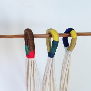 May include: Three macrame plant hangers with different colored yarn accents. The hangers are made of natural cotton cord and have a brown, yellow, and blue accent color.