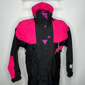 May include: A black and pink ski jacket with a hood. The jacket features a color-blocked design with pink shoulders and sleeves, a black center, and purple accents. It has a drawstring waist and a small logo on the sleeve.