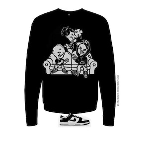 May include: Black sweatshirt with a white graphic of four cartoon characters sitting on a couch. The characters are wearing hats and have a playful expression. The text "etsy.com/shop/Recipracol" is printed on the right sleeve.