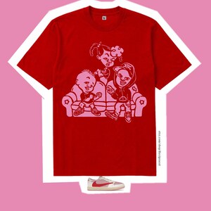 May include: A bright red short-sleeved t-shirt featuring a light pink graphic print of three cartoon characters sitting on a couch. The text etsy.com/shop/Recipracol is printed vertically on the lower right side. A single low-top sneaker is below.